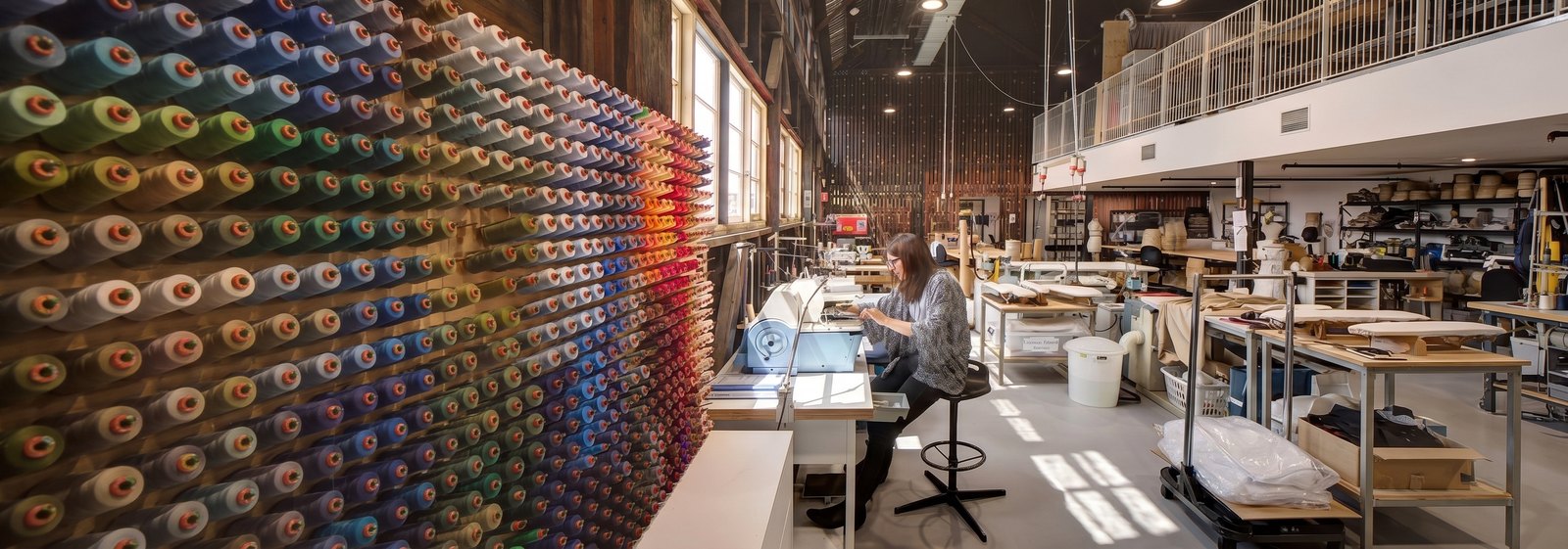 A workshop interior with a wall of coloured thread spools and a maker at a bench